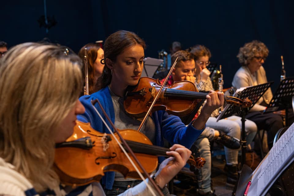 Geiger:innen in einem Orchester, die Bögen mitten in der Phrase gemeinsam erhoben