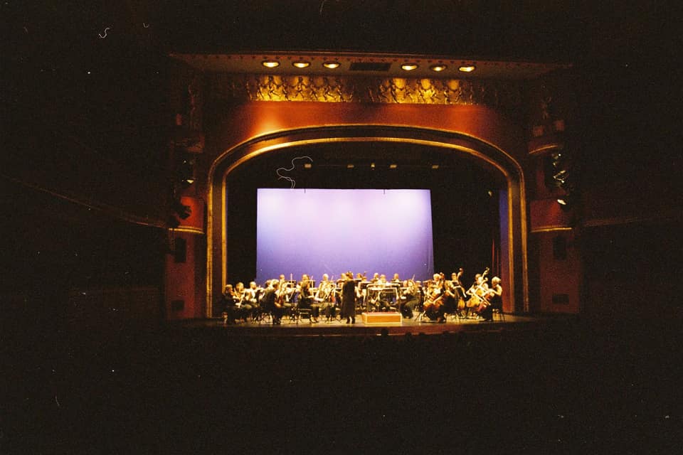 Ein Orchester spielt im dramatischen Scheinwerferlicht auf einer großen Bühne